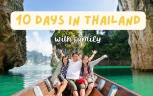 A family of three raising their arms in celebration while riding a long-tail boat on a serene lake surrounded by towering limestone karst mountains, with a travel graphic overlay "10 DAYS IN THAILAND with family.