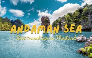 Andaman Thailand Travel Guide: A vibrant photo of the Andaman Sea coastline in Thailand, featuring a dramatic limestone karst island rising from the turquoise water, framed by lush green cliffs and a bright blue sky with white clouds. The text overlay reads "ANDAMAN SEA" and "Best travel tips in Thailand."