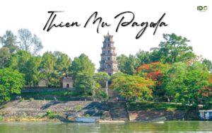 A travel postcard for Thien Mu Pagoda in Hue, featuring a scenic view from the Perfume River with a traditional dragon boat in the foreground. The iconic seven-story Phuoc Duyen Tower stands prominently on a hill, surrounded by lush green trees and vibrant red flame flowers.