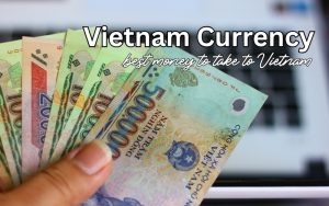 Hand holding a fan of Vietnamese dong banknotes in various denominations, with text overlay "Vietnam Currency: best money to take to Vietnam."