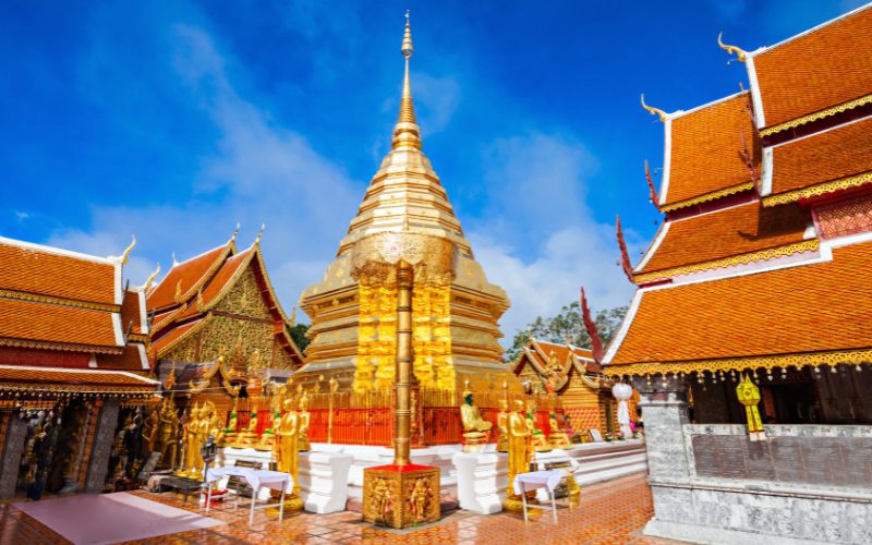 Golden stupa of Wat Phra That Doi Suthep in Chiang Mai surrounded by ornate temple buildings under a bright blue sky